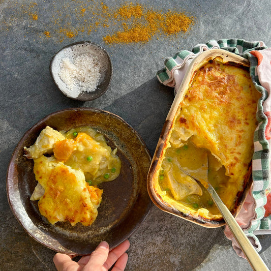 Hand holding plate of creamy chicken pie with mashed potato crust and peas and carrots