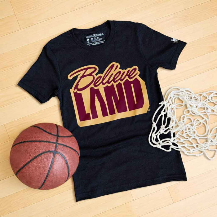 Black t-shirt with 'Believe Land' design on a wooden floor with a basketball and net.