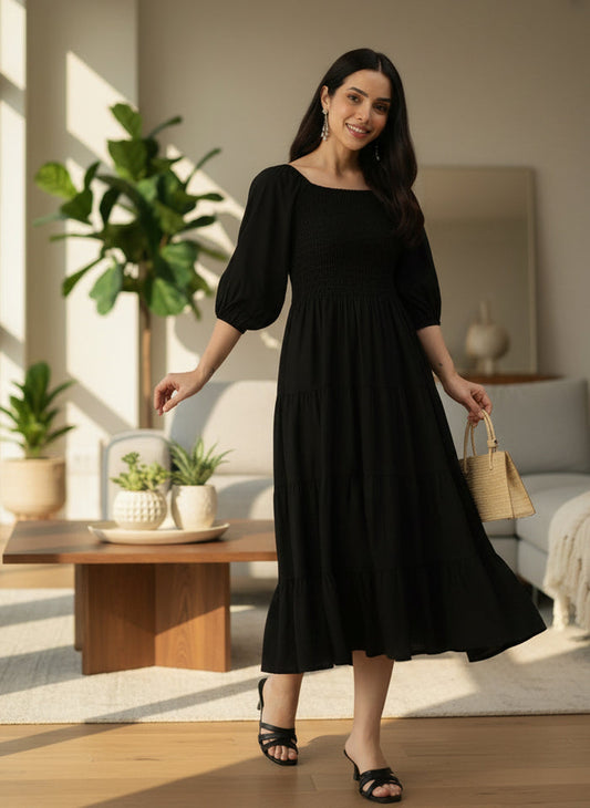 Woman in a black dress standing in a bright living room with plants and furniture. Black Solid Cuffed Sleeves Dress, midi dress, dress, women’s western wear, party wear dress, casual wear dress