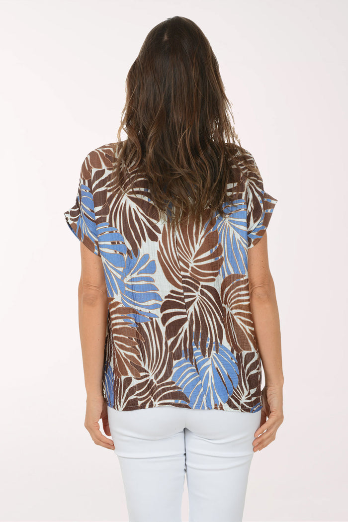 Woman wearing a patterned top with brown, blue, and beige leaves on a white background