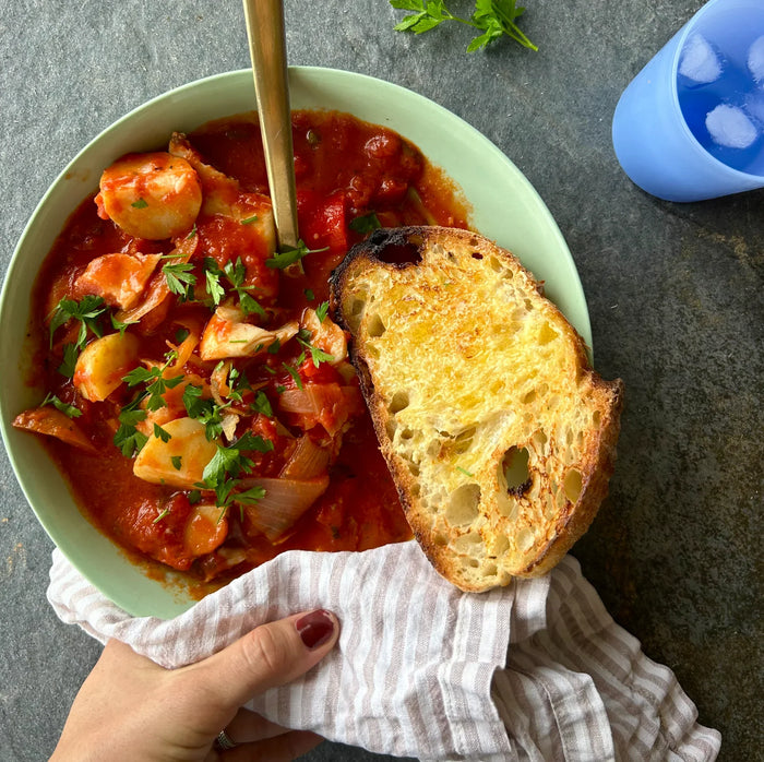 A bowl of Fish Provencal stew with potatoes and herbs, served with a slice of bread.