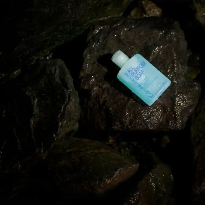 A 200ml bottle of Life Venture All Purpose Liquid Soap with a translucent light blue body and a white cap, placed on a rock in water.