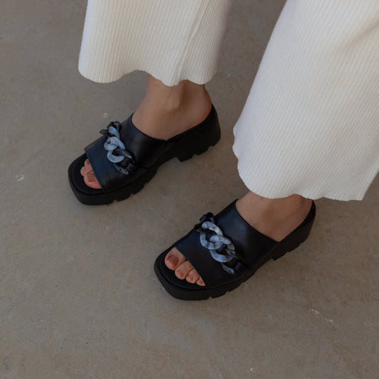 Black sandals with floral straps worn by a person on a neutral background