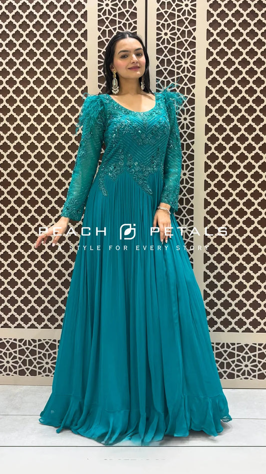 Teal floor-length pleated gown featuring intricate bodice embroidery and dramatic feather-trimmed shoulders with long sleeves.