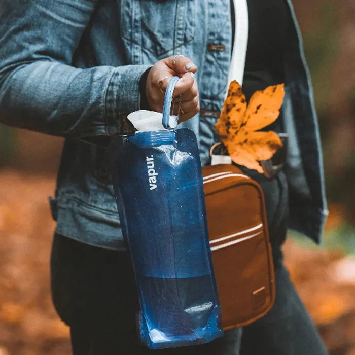 Lifestyle image of a woman carrying a Vapur Eclipse anti water bottle using the carabiner handle during autumn